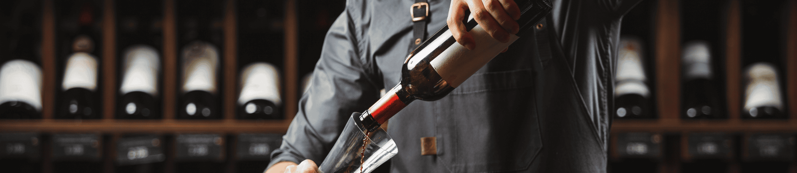 Person pouring wine at a wine cellar with bottles in the background.